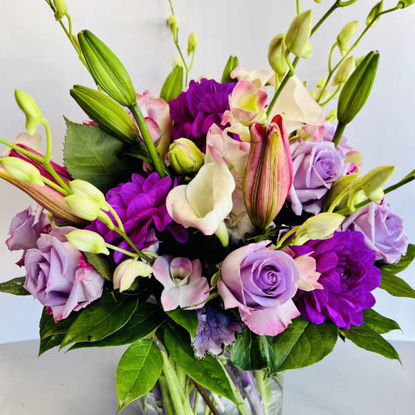 Bouquet of purple roses, lilies, and calla lilies in a glass vase