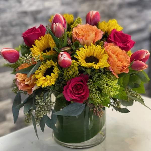 Mixed bouquet in a glass vase with roses, sunflowers, tulips, and carnations