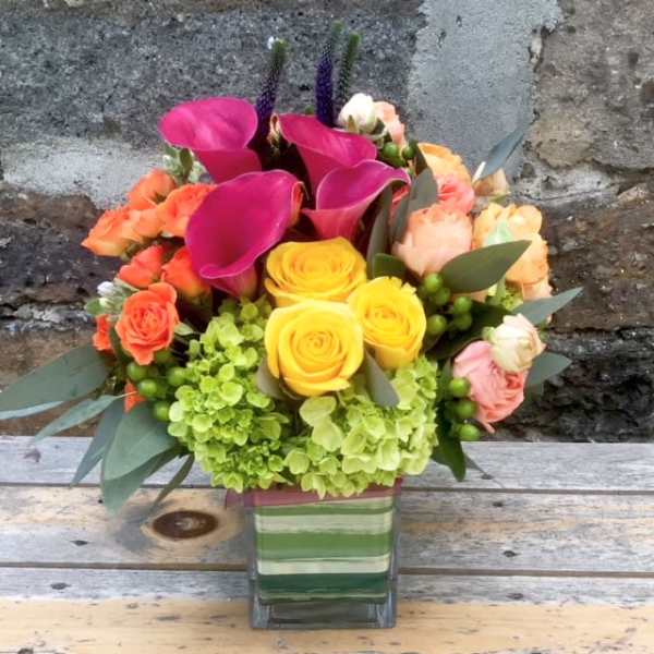 Colorful bouquet with pink calla lilies, yellow roses, and green hydrangeas in a glass vase
