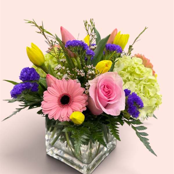 Mixed bouquet in a square glass vase with pink and yellow blooms