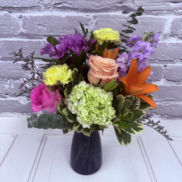 Mixed bouquet in a dark vase with roses, hydrangea, lilies, and purple blooms