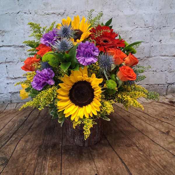 Colorful bouquet with sunflowers, roses, and purple blooms in a rustic wood container