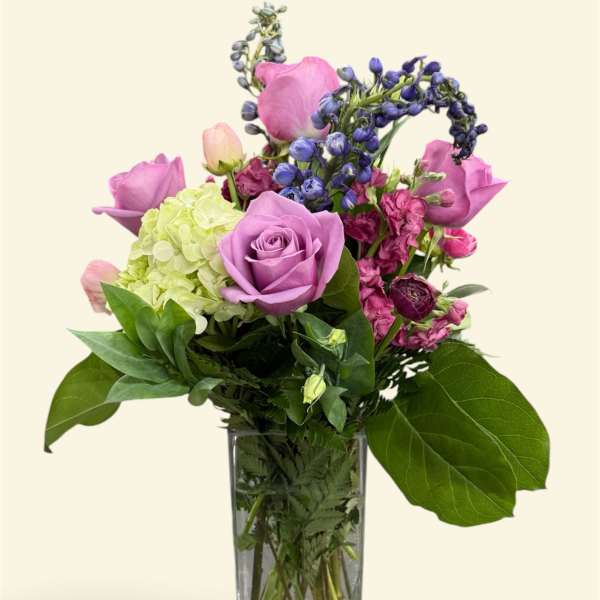 Lavender roses and mixed purple flowers in a clear glass vase
