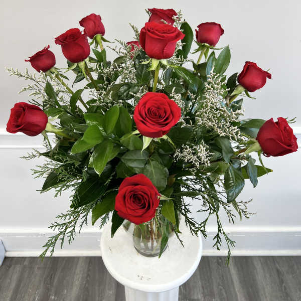 Arrangement of long-stem red roses with small white filler flowers in a clear glass vase