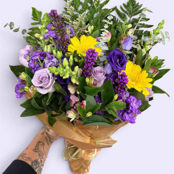 Hand-tied bouquet of purple and yellow flowers wrapped in brown paper