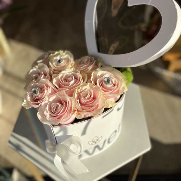 Pink roses in a white heart-shaped box with a ribbon bow