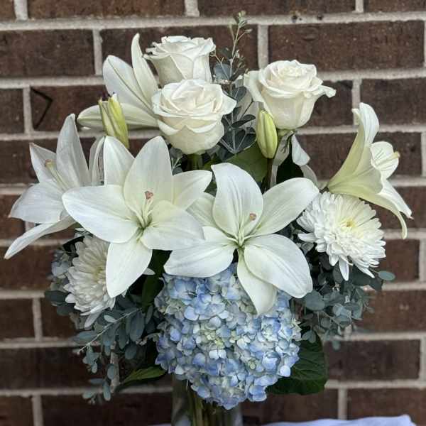 White lilies and roses with blue hydrangea in a glass vase
