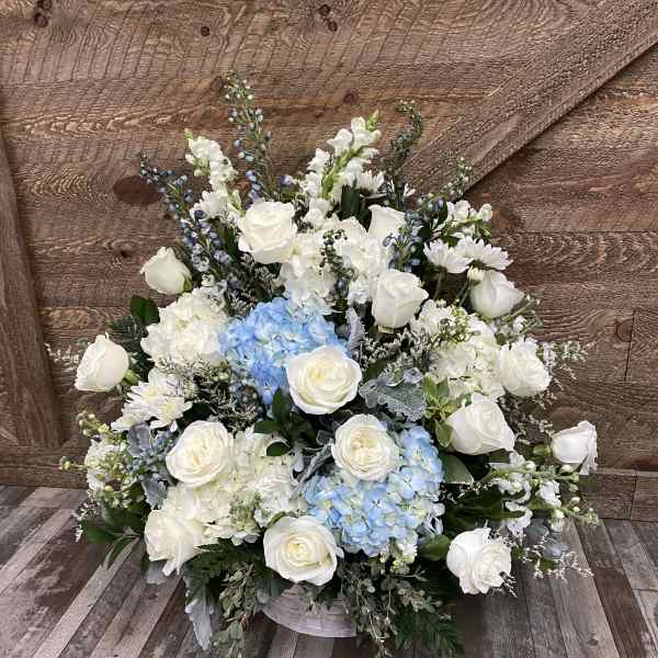 Large white floral arrangement with blue hydrangeas in a low container
