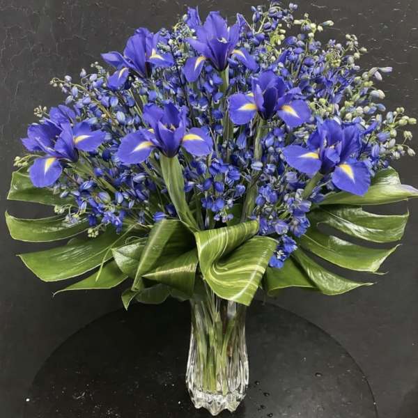 Blue iris bouquet in a clear glass vase with broad green leaves