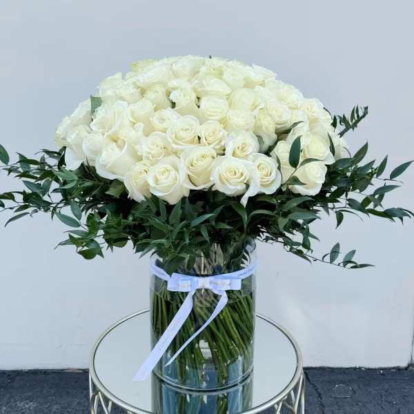 Large bouquet of white roses in a clear glass vase with a ribbon