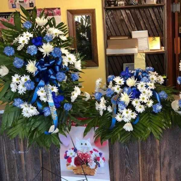Three blue-and-white floral wreaths with ribbons on stands