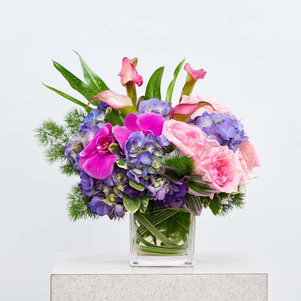 Pink orchids and roses with purple hydrangeas in a clear glass vase