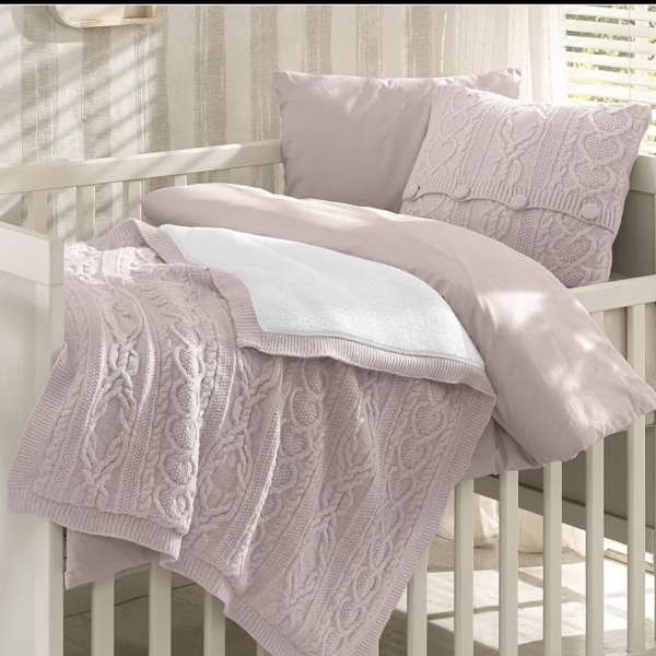 Pastel knit blanket and pillows arranged on a white crib