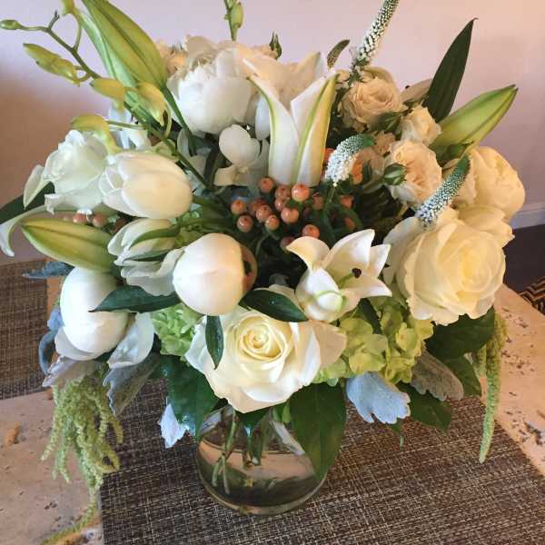 White floral arrangement in a glass vase with roses and lilies