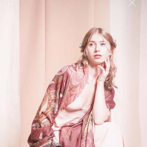 Woman wearing a pink floral shawl and pale dress against a soft pink backdrop