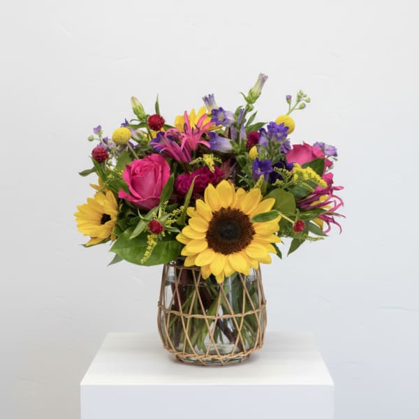 Mixed bouquet with sunflowers, pink roses, and purple flowers in a glass vase