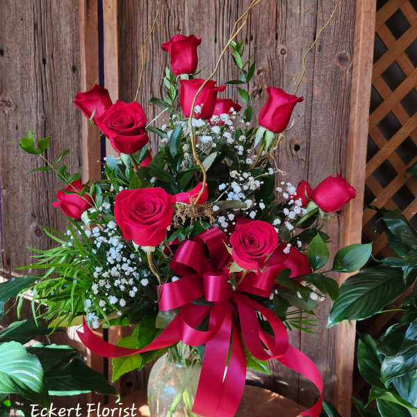 Red roses arranged in a clear glass vase with a red ribbon bow