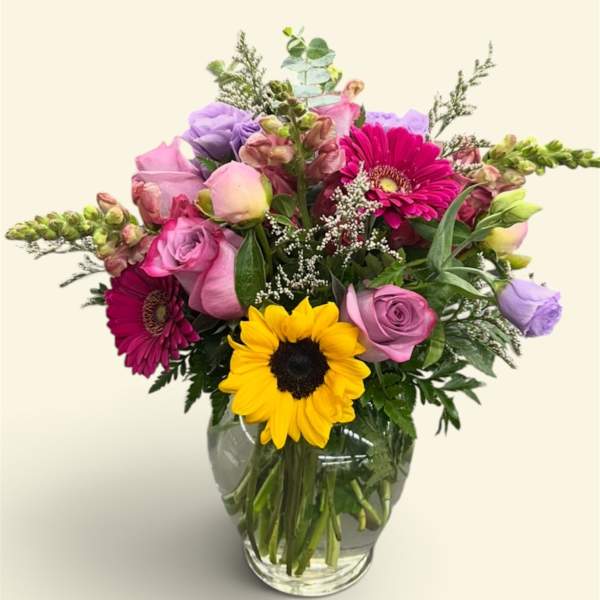 Mixed bouquet in a glass vase with sunflowers, roses, and pink gerberas
