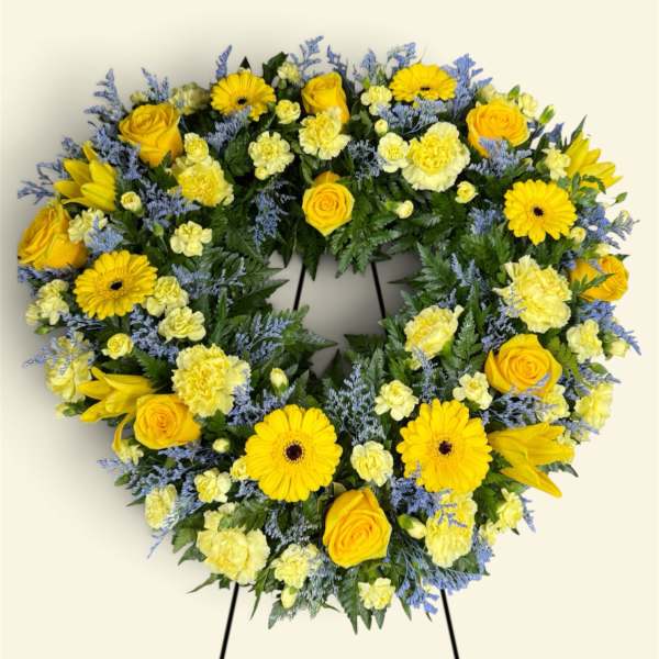 Heart-shaped floral wreath with yellow roses and daisies on a stand