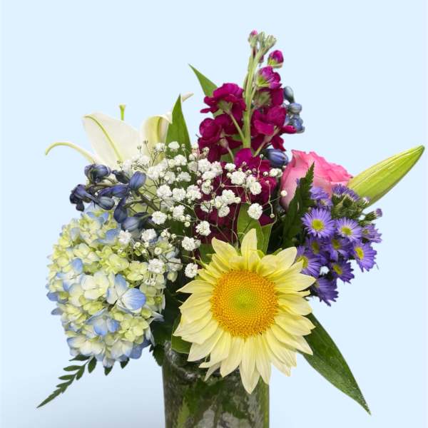 Mixed bouquet in a glass vase with a yellow sunflower, pink rose, and purple blooms