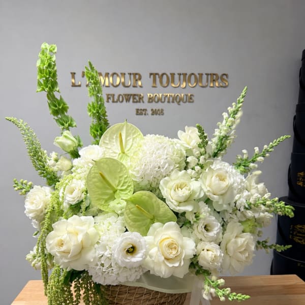 White floral arrangement in a wicker basket with green accents