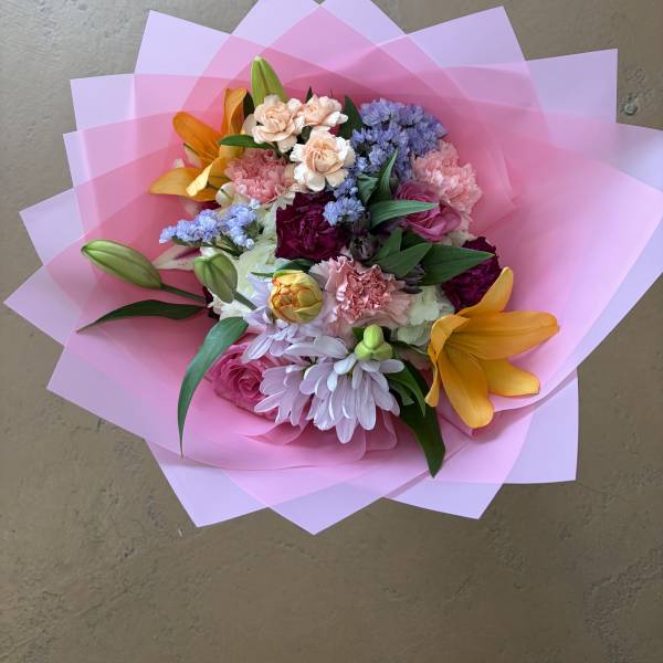 Mixed bouquet with pink, purple, and orange flowers wrapped in pink paper
