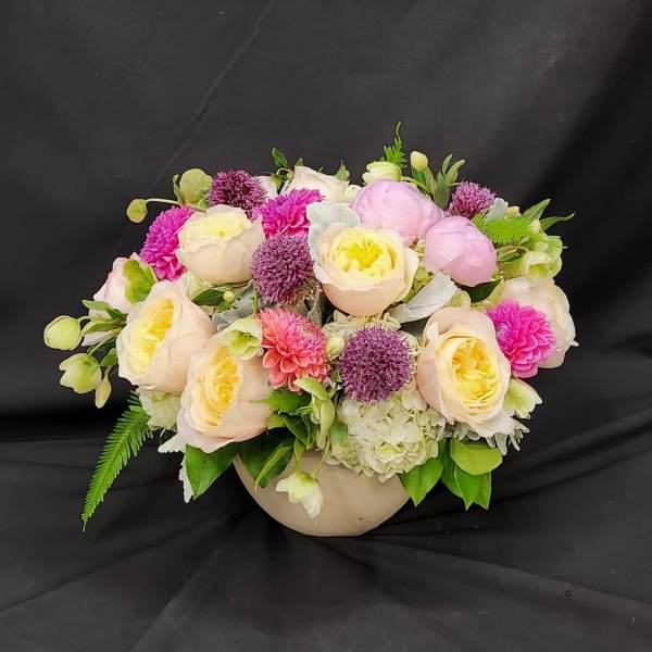 Low floral arrangement of pale roses, pink blooms, and purple accents in a round vase
