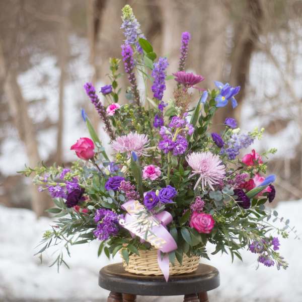 Basket arrangement of purple and pink flowers with a lavender ribbon
