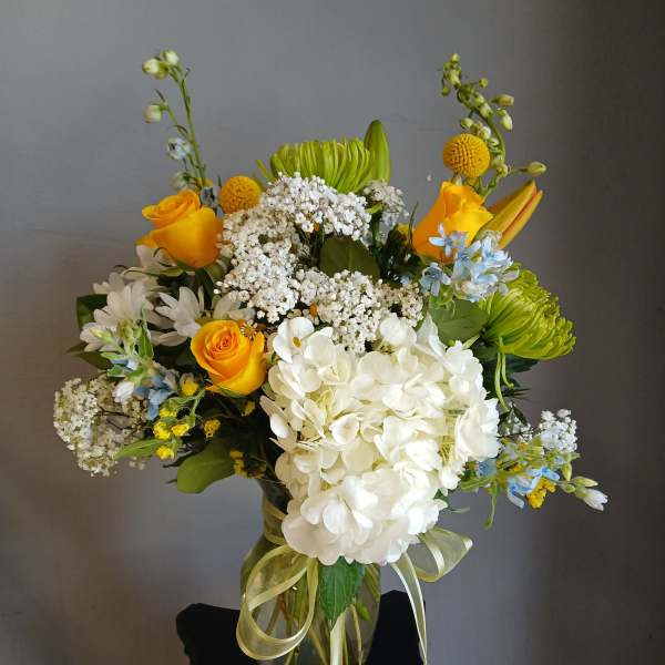 Mixed bouquet of yellow roses, white hydrangea, and green chrysanthemums in a glass vase