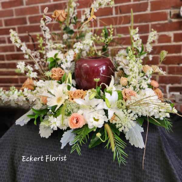 Low floral arrangement with white lilies, peach roses, and white daisies in a burgundy vase