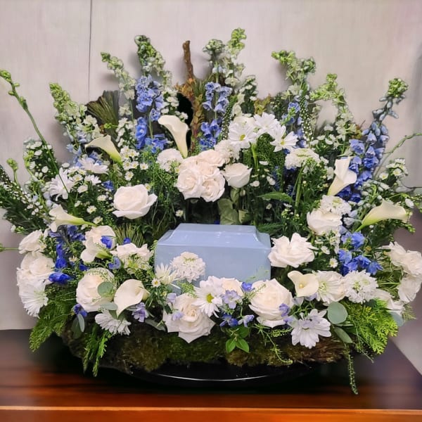 Large floral funeral arrangement with white roses, calla lilies, and blue flowers