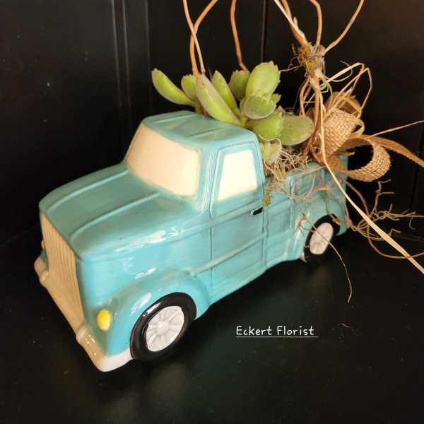Succulent arrangement in a turquoise ceramic truck planter with a small bird topper
