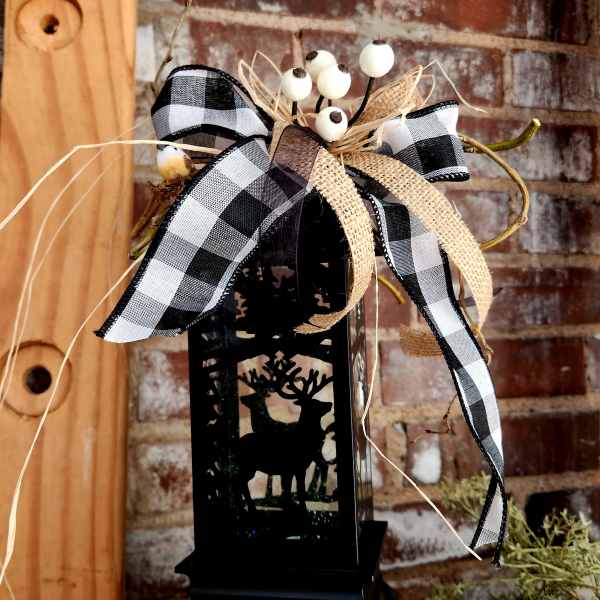 Black lantern with deer cutout topped by a plaid bow and white berries