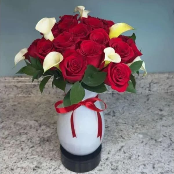 Bouquet of red roses and white calla lilies in a white vase with a red ribbon