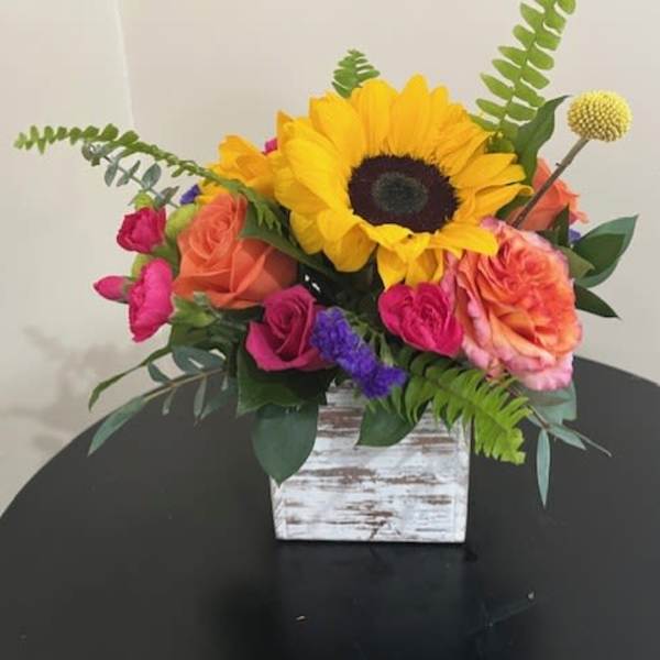 Bright sunflower and mixed roses in a whitewashed wooden cube vase