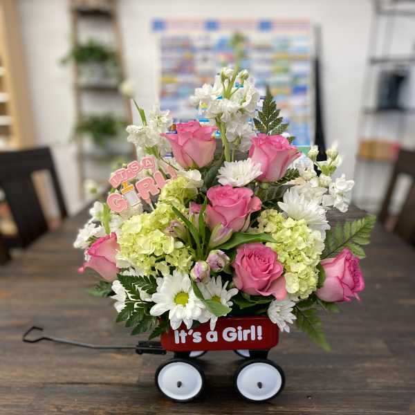 Pink roses and white flowers in a red wagon with an "It's a Girl!" sign