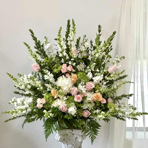 Large floral arrangement with pink and peach roses, white blooms, and greenery in a pedestal vase