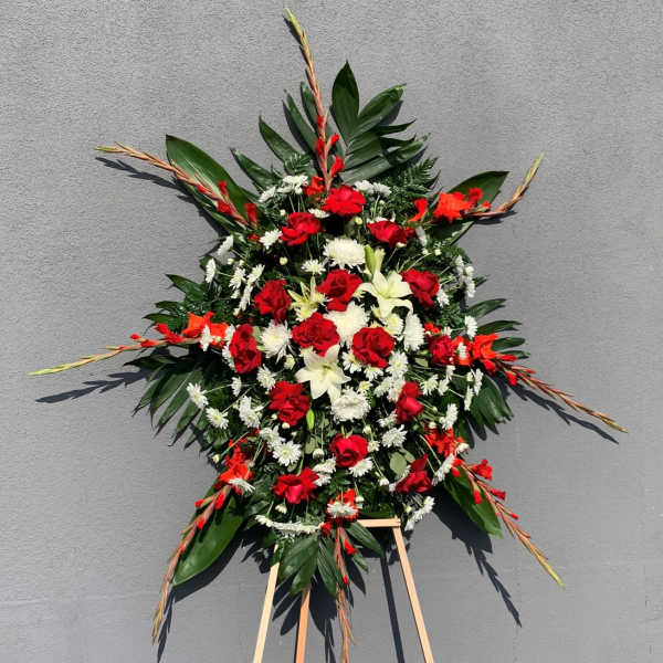 Standing floral spray with red roses, white lilies, and daisies on an easel