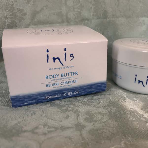 Box and jar of Inis body butter on a patterned fabric surface