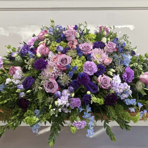 Large purple and pink floral casket spray with trailing greenery