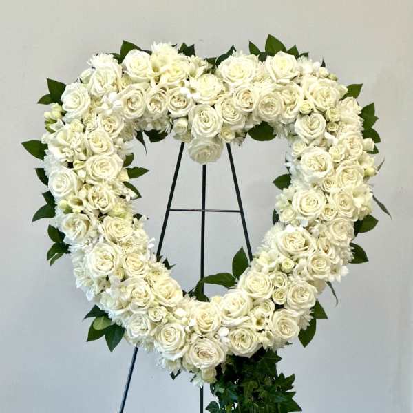 Heart-shaped white floral wreath on a stand with trailing ivy