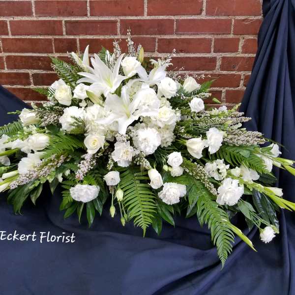 White funeral spray with lilies and roses on dark drape