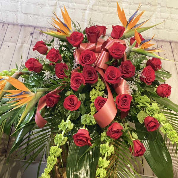 Large bouquet of red roses with orange bird-of-paradise blooms and pink ribbon