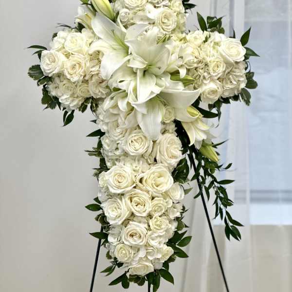 White floral cross on a stand with lilies and roses