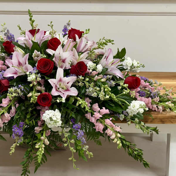 Long floral arrangement with red roses and pink lilies on a wooden table