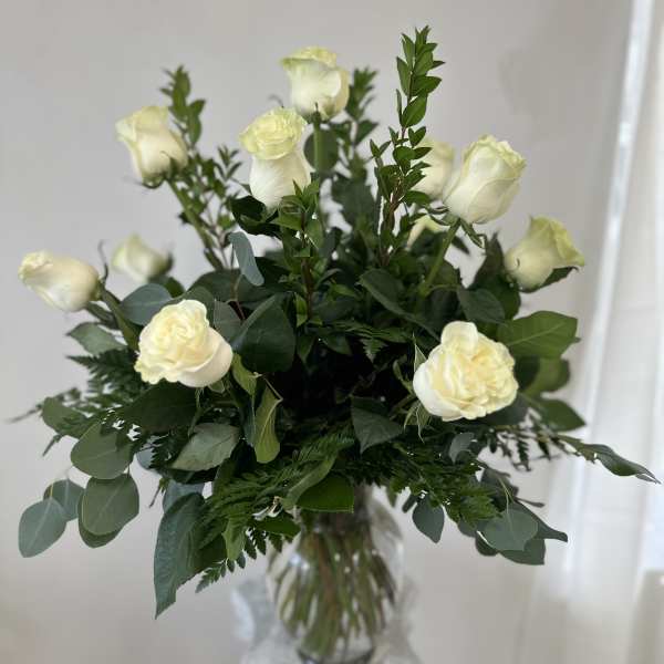 White roses arranged in a clear glass vase with mixed greenery