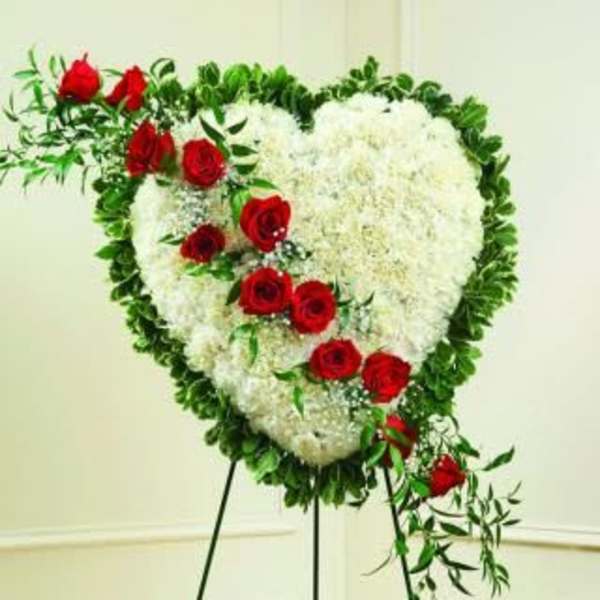 Heart-shaped white floral wreath with red roses on a stand