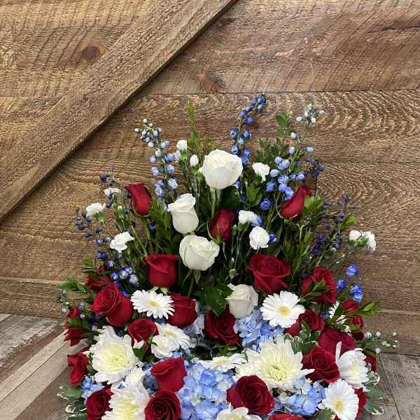 Red and white roses with blue flowers and white daisies in a low arrangement