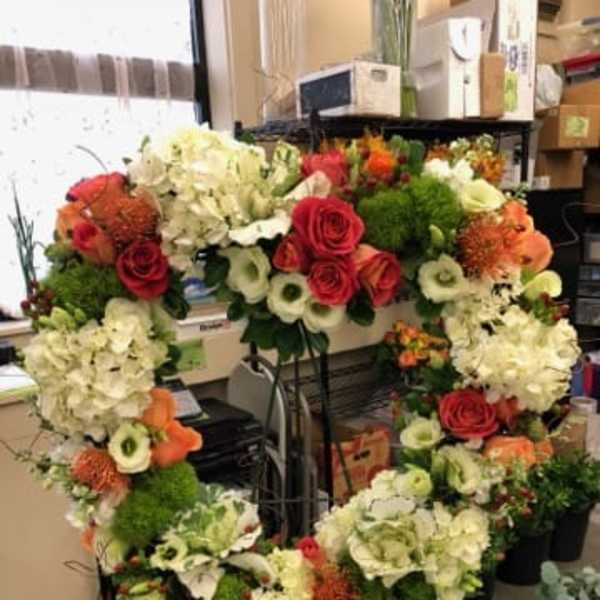 Large floral wreath with red roses, white hydrangeas, and orange blooms