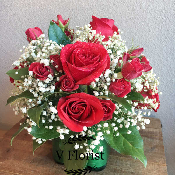 Compact arrangement of red roses and baby's breath in a green glass vase